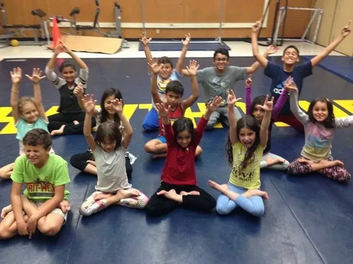 Children sitting together on mats after a Yoga Angels kids class, arms raised