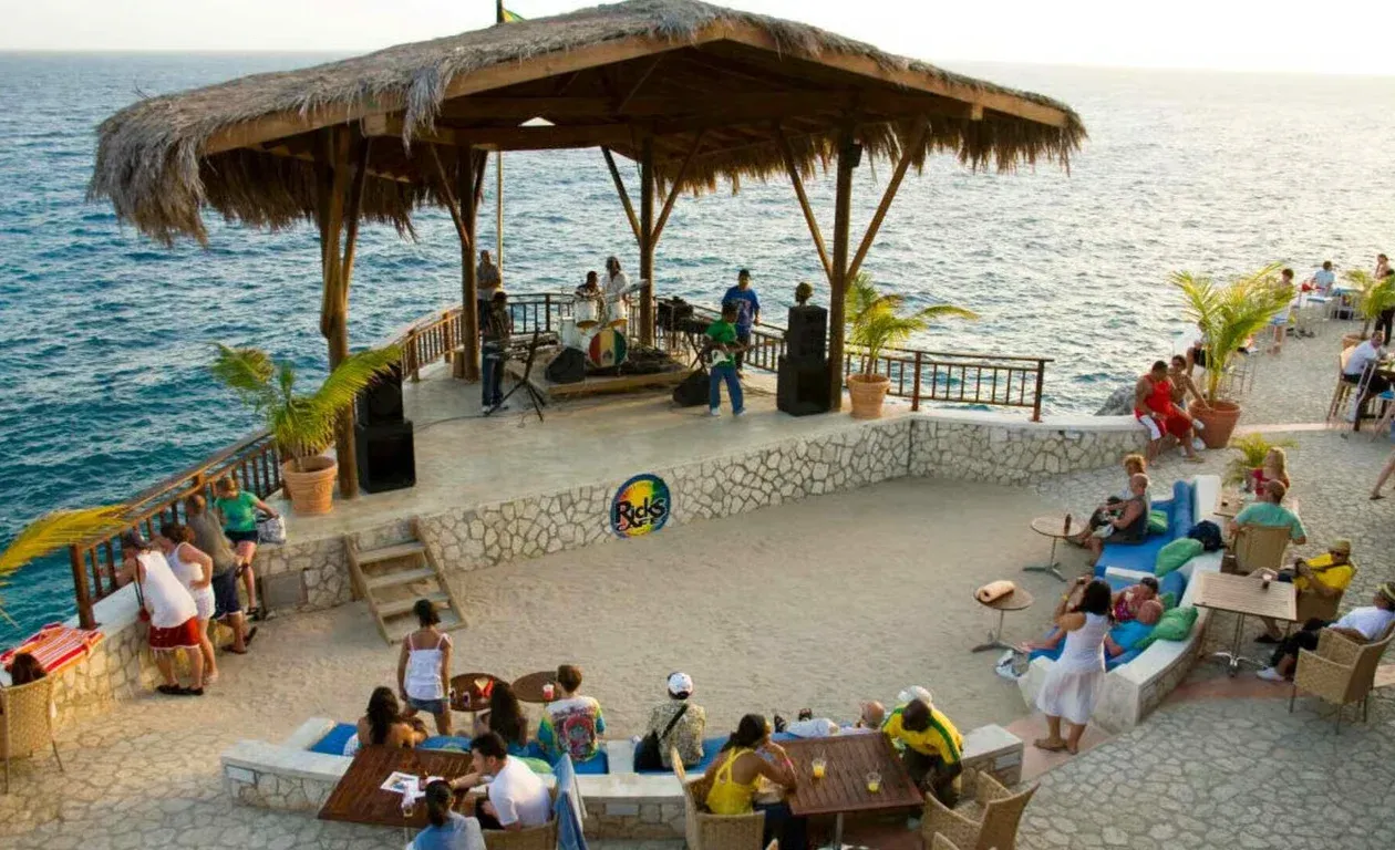 Guests gathered on a seaside terrace under a thatched roof, the Caribbean behind them